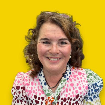 Photograph of Dr Sharryn Gardner. She is smiling on a yellow background and wearing a multicoloured summer dress
